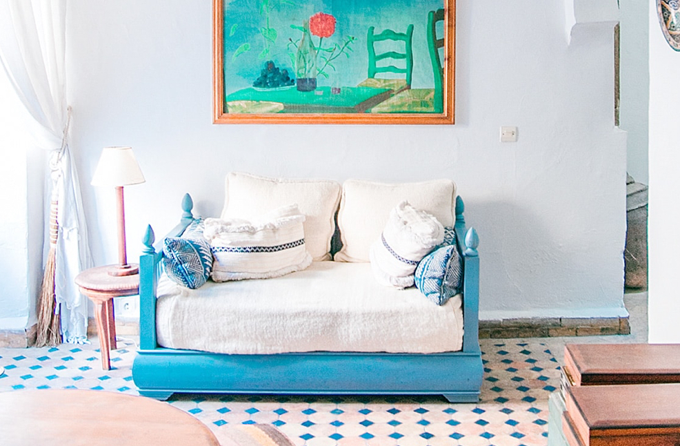 A living space with a aqua coloured sofa bed against a wall under a painted of a painted rose on a table.