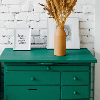 A green painted dresser with two picture frames and a milk jub with wheat.