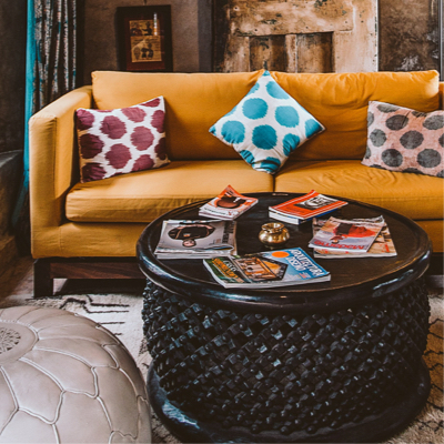 Living space with a yellow couch that has 3 polka dot pillows and around coffee table full of magazines.